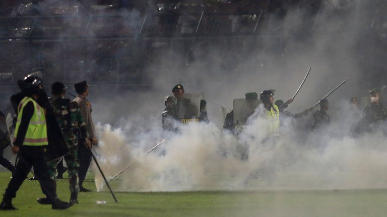 Police officers and soldiers stand amid tear gas smoke after clashes between fans during a soccer match at Kanjuruhan Stadium in Malang, East Java, Indonesia, Saturday, Oct. 1, 2022. Panic following police actions left over 100 dead, mostly trampled to death, police said Sunday. (AP Photo/Yudha Prabowo)